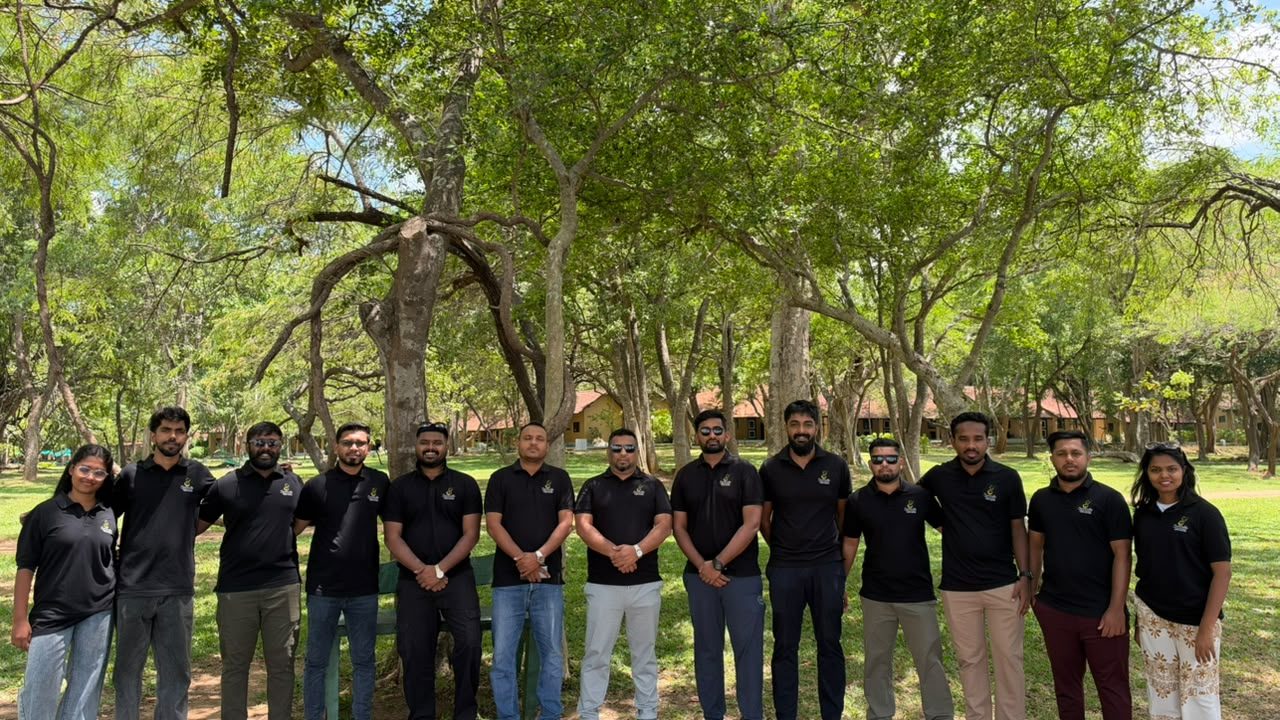The Serendib Travel Holidays team in matching black polo shirts, standing together under trees on a team day out
