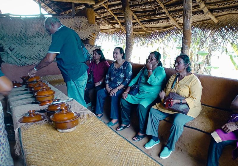 A host lifting the lids of clay cooking pots for guests in a thatched hut
