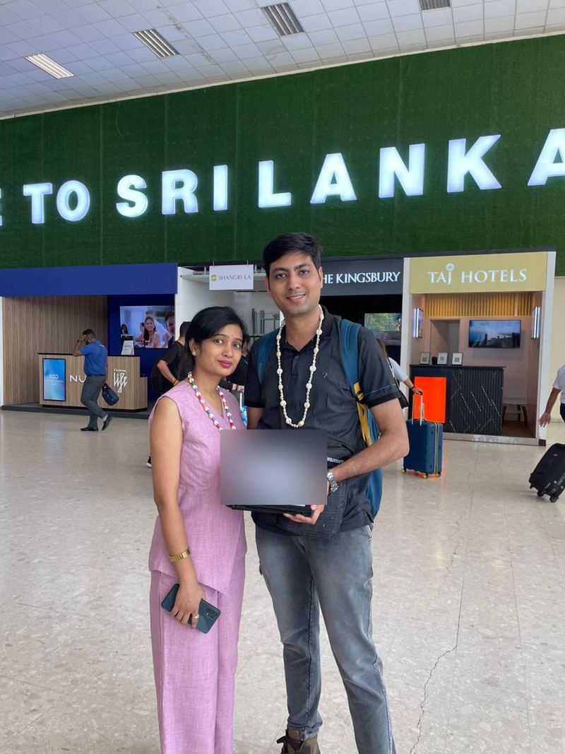 A couple with shell garlands under the Welcome to Sri Lanka sign