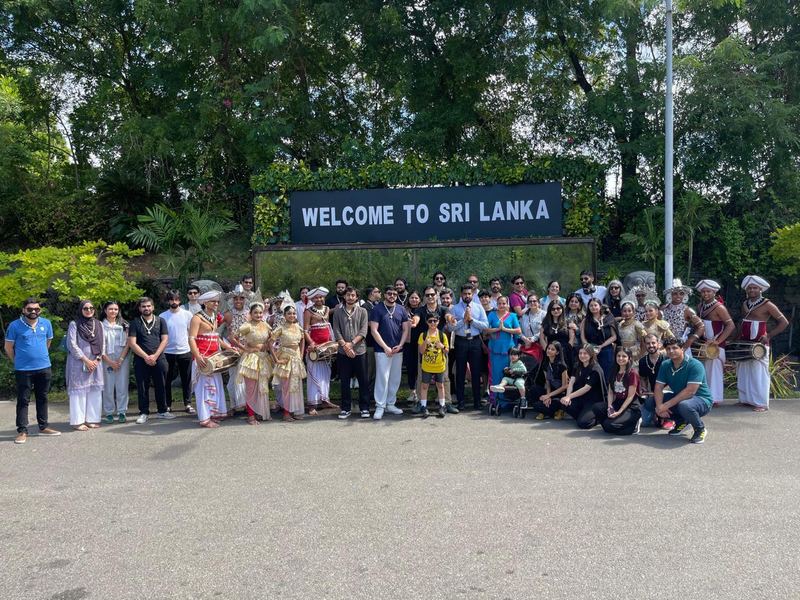 A large group with dancers and drummers in front of the Welcome to Sri Lanka sign
