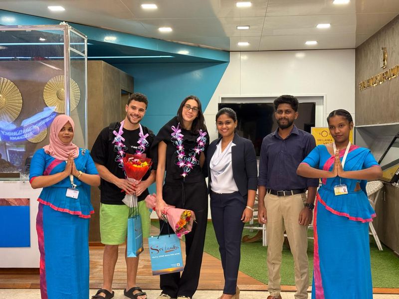 A couple with orchid garlands and bouquets, welcomed by staff at the Sri Lanka Tourism desk