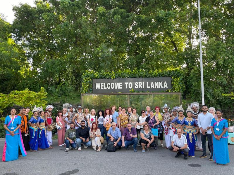 A tour group with dancers and drummers under the Welcome to Sri Lanka sign