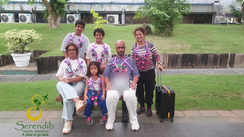 A family of six with orchid garlands on a bench outside the airport