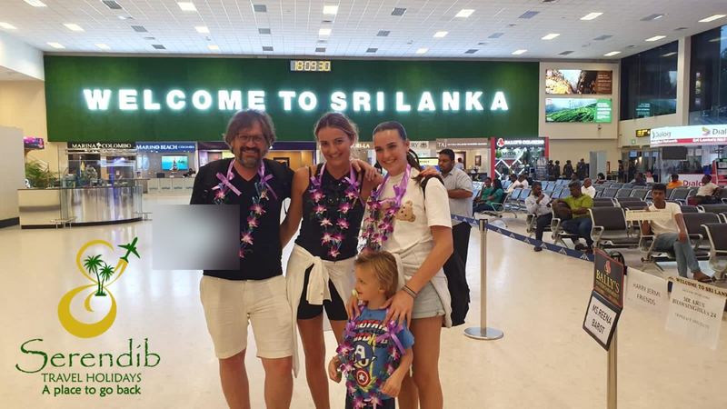 A family with orchid garlands under the Welcome to Sri Lanka sign