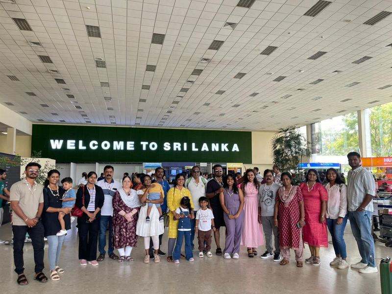 A large family group with shell garlands under the Welcome to Sri Lanka sign