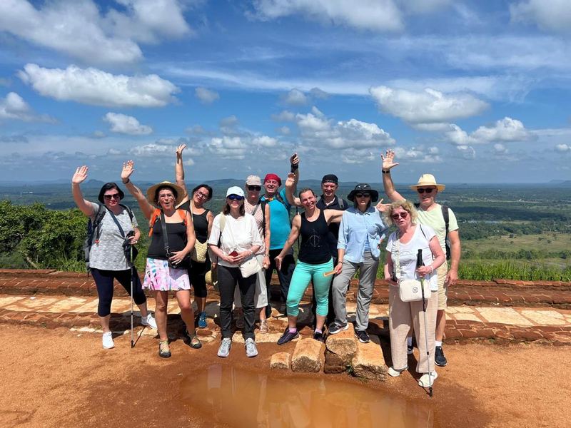 A tour group waving at the summit of Sigiriya rock with forest plains behind them