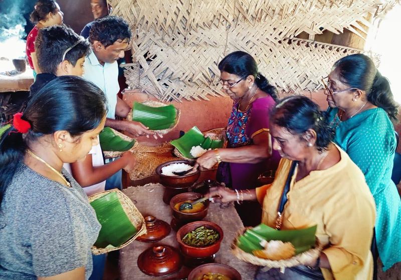 Guests serving themselves rice and curry from clay pots onto banana leaves